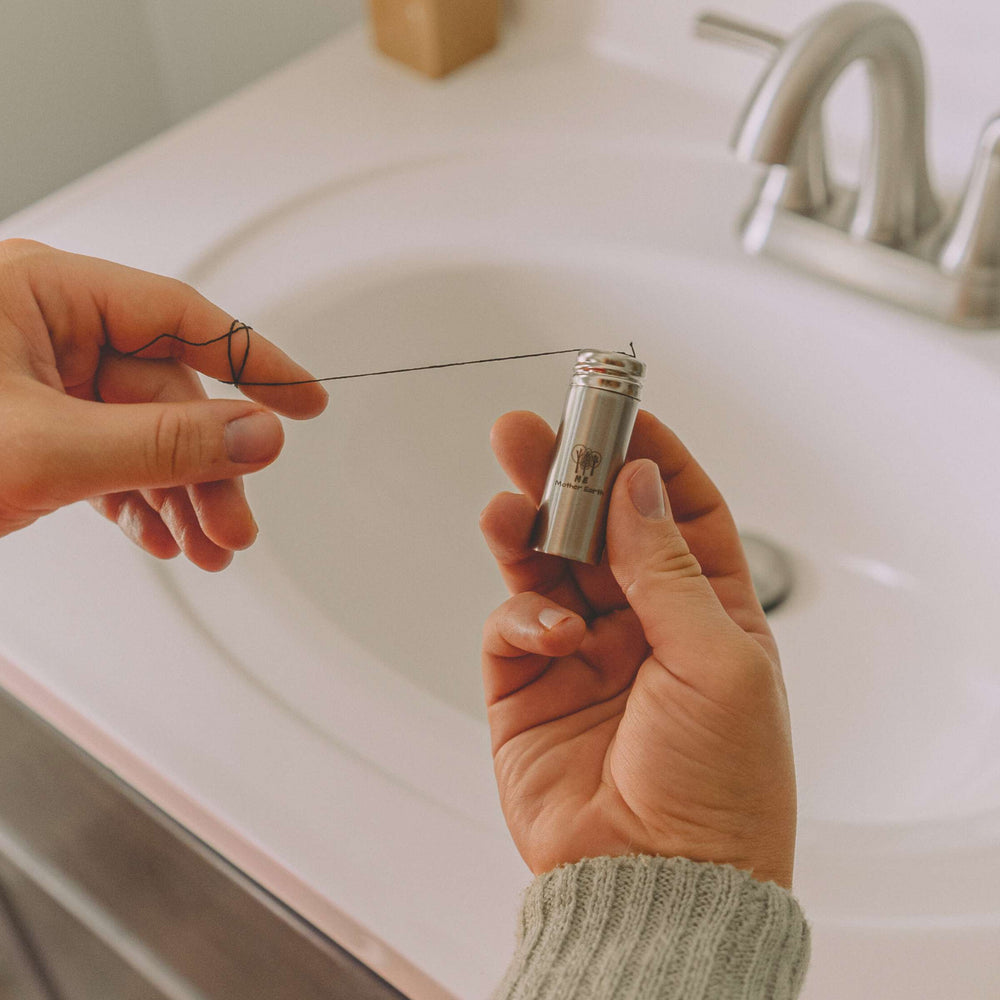Bamboo charcoal fiber dental floss in stainless steel container, in use above sink.