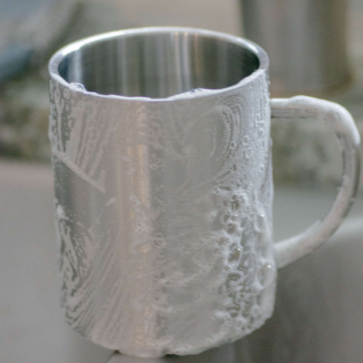Stainless steel mug covered in suds made from solid dish detergent block.