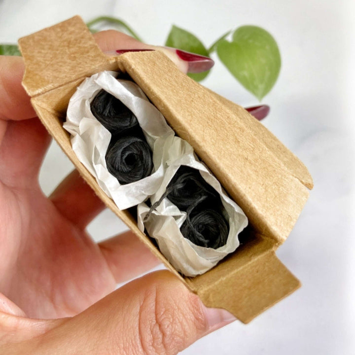 ME Mother Earth Charcoal Dental Floss 4-pack Refills Open Box Held in Woman's Hand with Houseplant in Background.