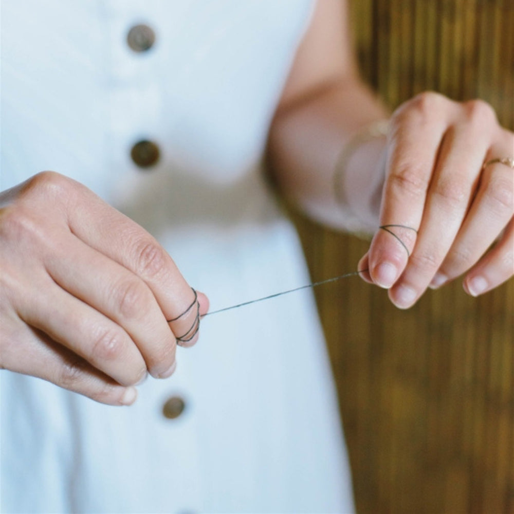 ME Mother Earth Charcoal Dental Floss 4-pack Refills Single Piece Shown in Hands of Woman Wearing a White Dress.
