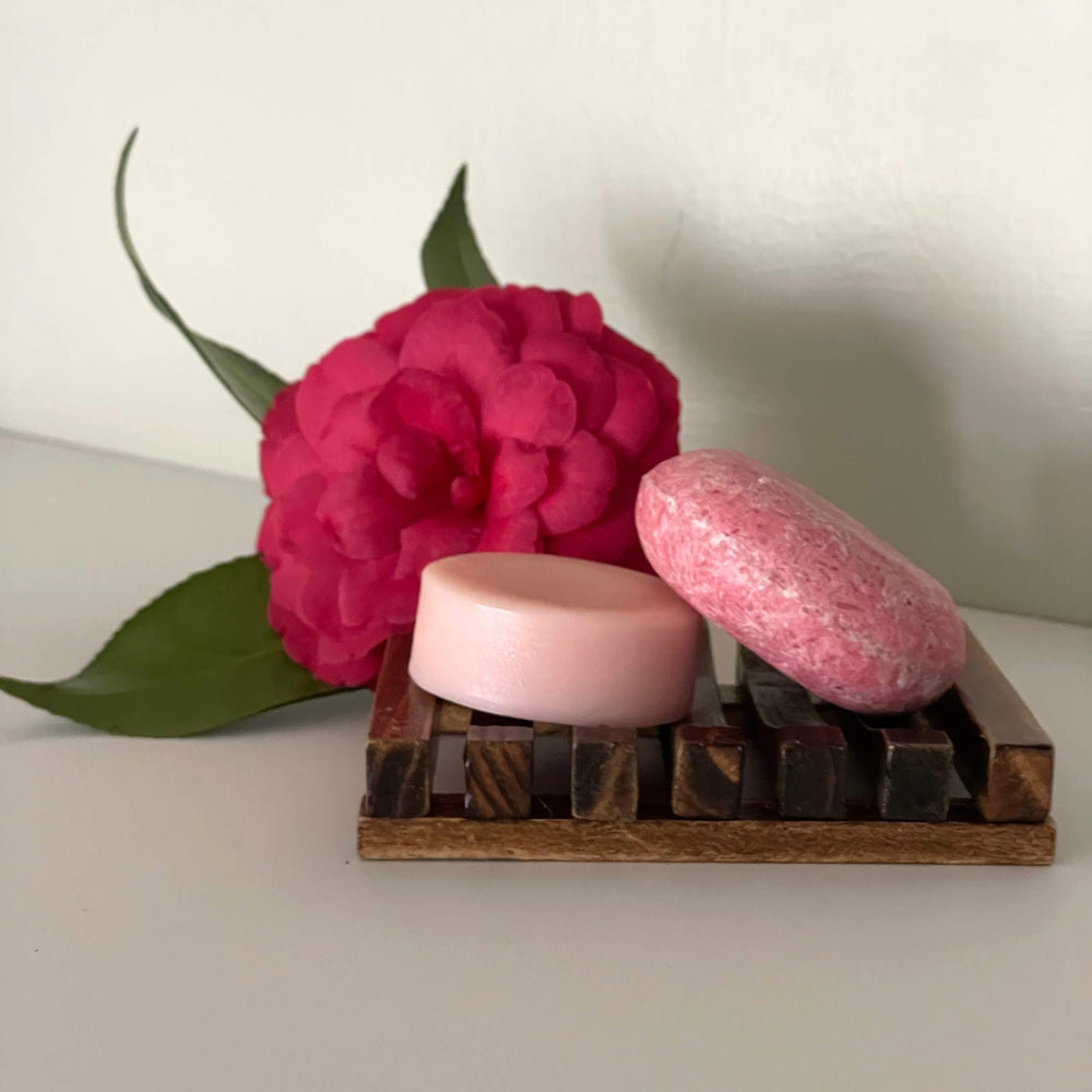Humby Shampoo Bar and Humby Conditioner Bar in Vanilla Coconut scent on wood soap shelf with pink flower in background.
