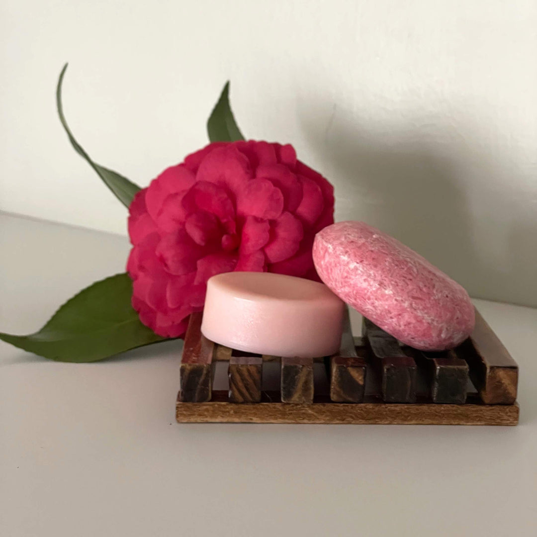 Humby Shampoo Bar and Humby Conditioner Bar in Vanilla Coconut scent on wood soap shelf with pink flower in background.