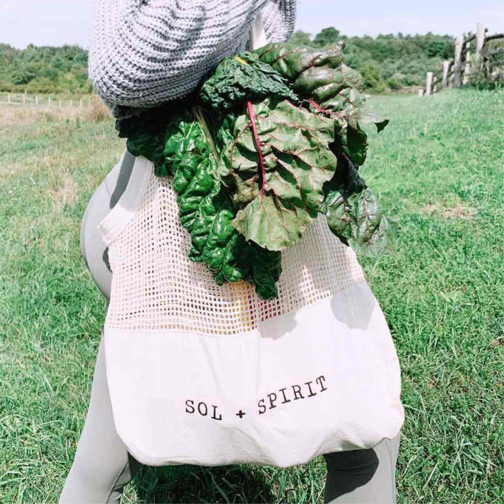  Canvas Sling Shopping Bag on woman's arm with greens in bag. Green grass field in background.