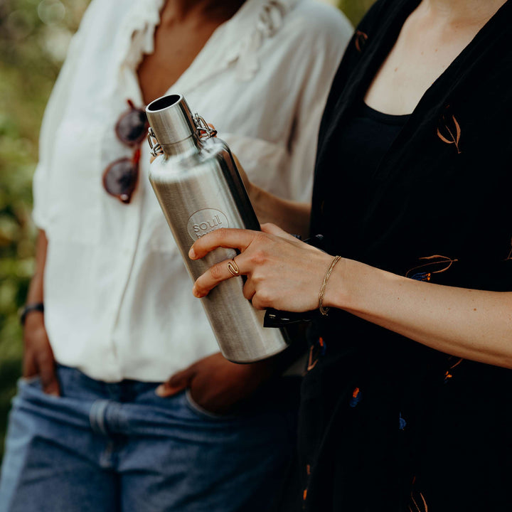 Soulbottles stainless steel light bottle in Basic (no added color), 25 ounce capacity, held in woman's hand with another woman walking beside.