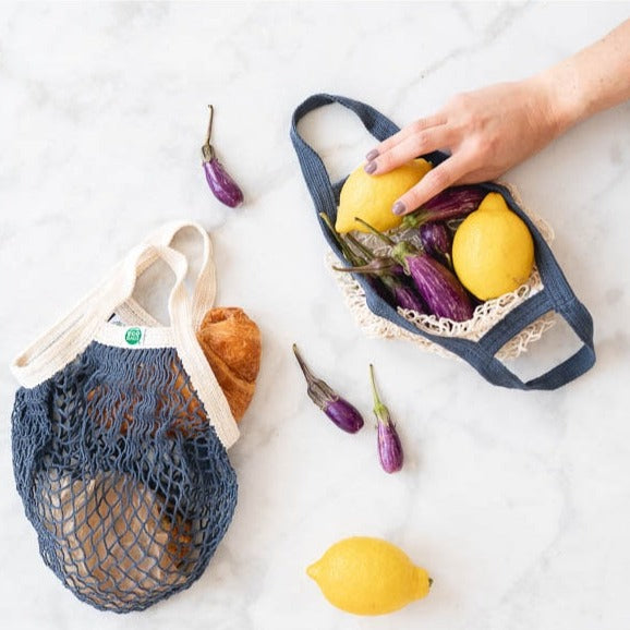 EcoBags Mini String Bag In Storm Blue, Shown With Woman Reaching For Lemon In Bag.