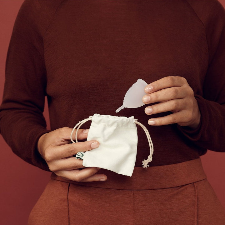 Woman dressed in red and orange, holding AllMatters Menstrual Cup And Storage Pouch.